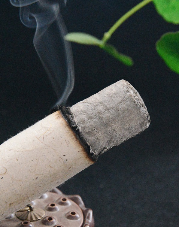Smoke and grey ash on the burning end, resting on a moxa holder (manufacturer detail photo).